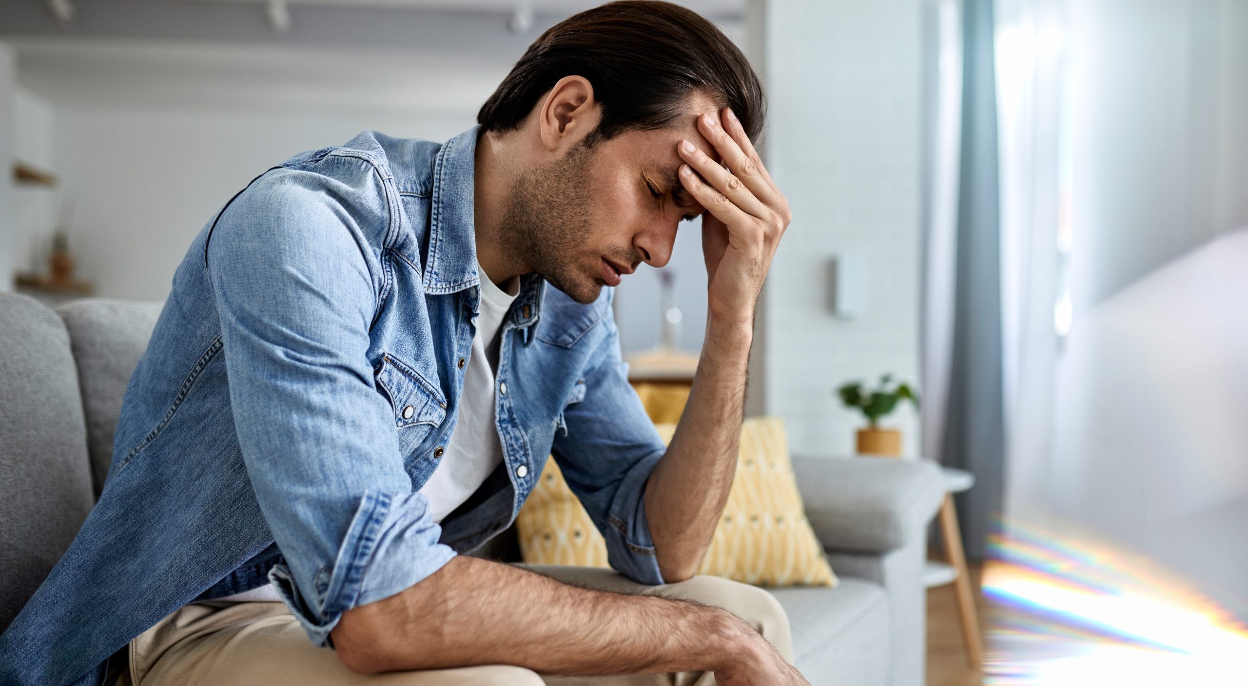 Young man having a headache and holding his head in pain at home.